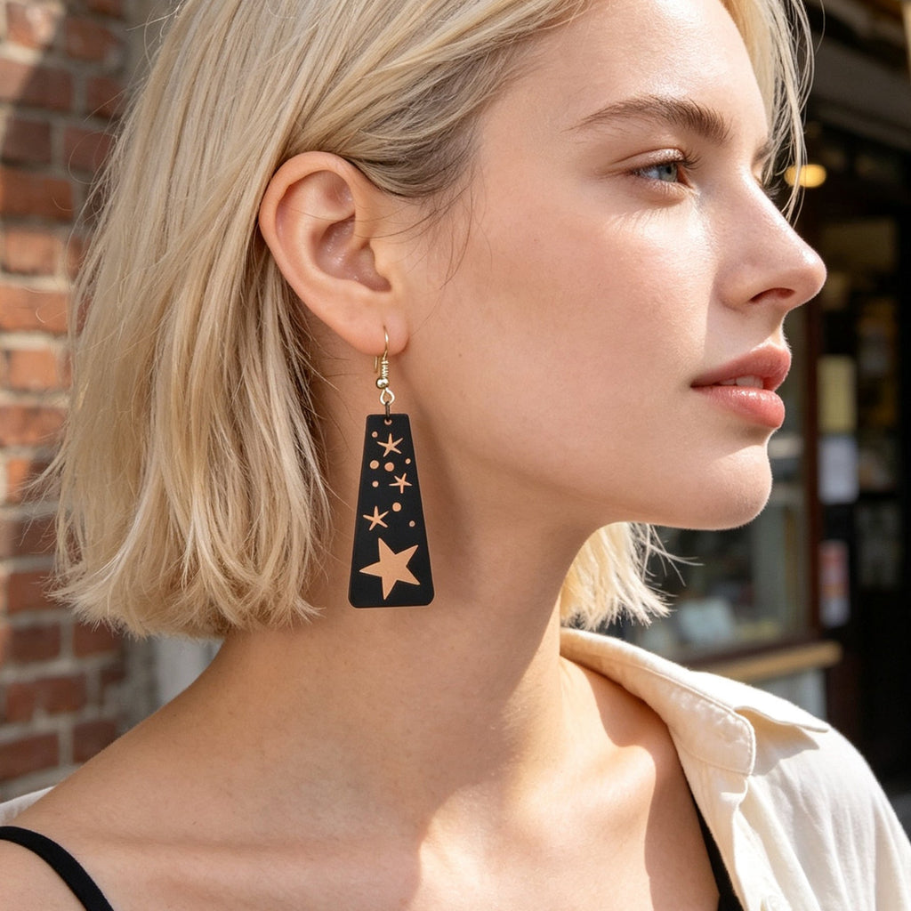 Black starry sky dangle earrings with moon and star cutouts, dangling from gold-tone hooks