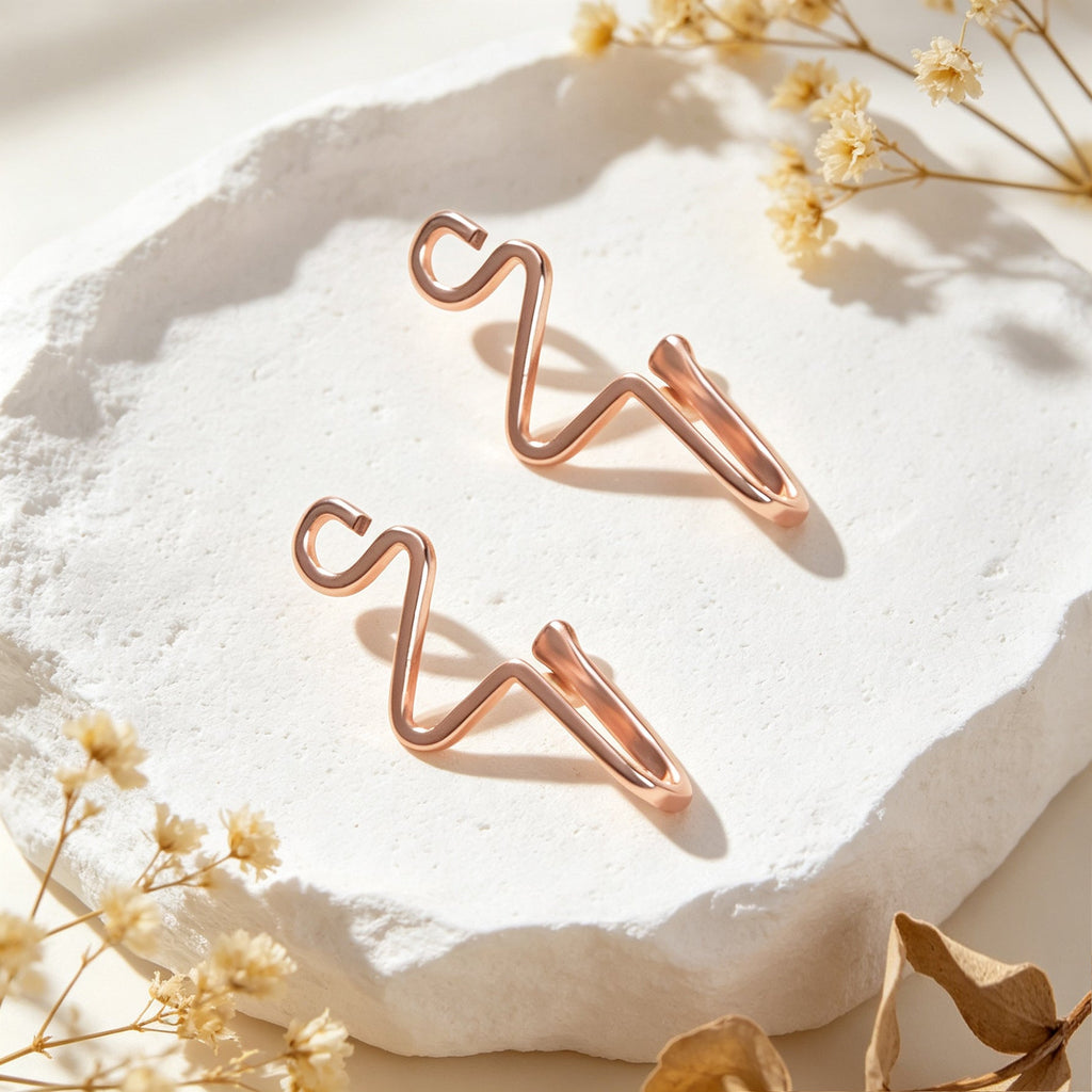 Rose gold wave ear cuffs, set of two, laid on white stone