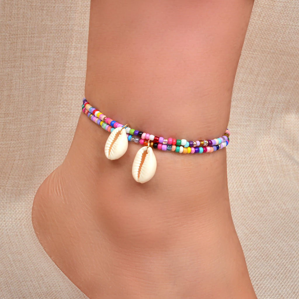 Ankle wearing two multicolor bead bracelets with white cowrie shell charms
