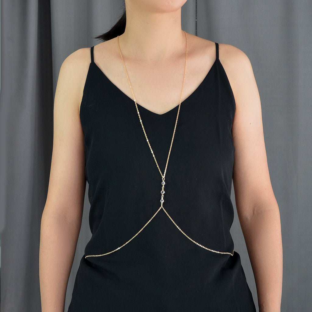 Gold-tone body chain harness draped over black V-neck camisole with charm centerpiece