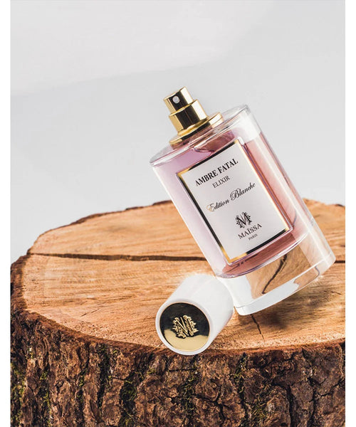 Perfume bottle with clear glass body, gold top, and pink-tinted label reading Edition Blanche