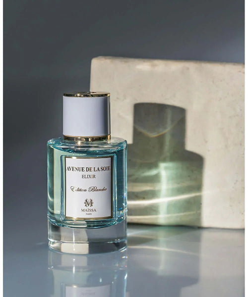 Gold-capped glass perfume bottle with pale blue liquid, label facing camera