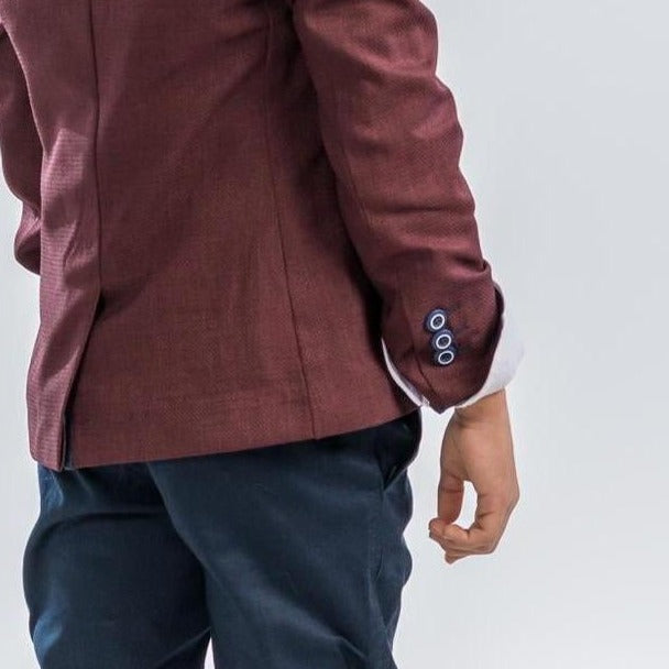 Boys burgundy blazer sleeve with button cuff detail, paired with dark trousers
