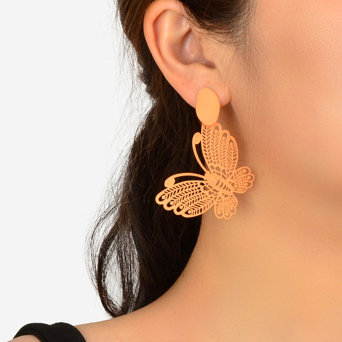 Orange hollow butterfly stud earrings with filigree leaf charm, worn on ear