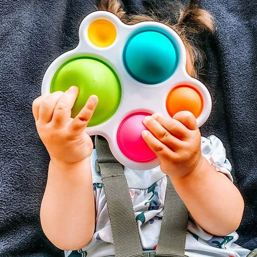 Baby rattle puzzle toy with six colored circles; child hands pressing the bumps