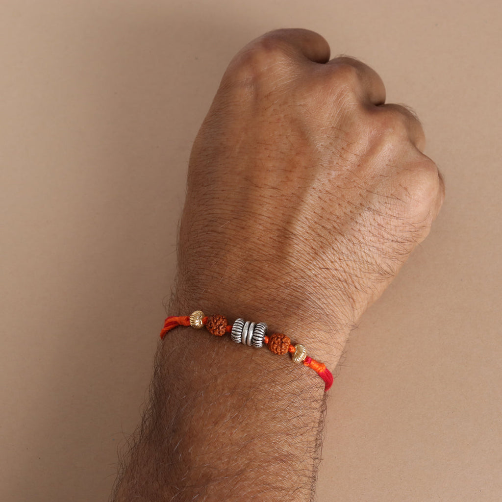 Rakhi worn on wrist: red–orange thread with rudraksha beads and silver barrel bead