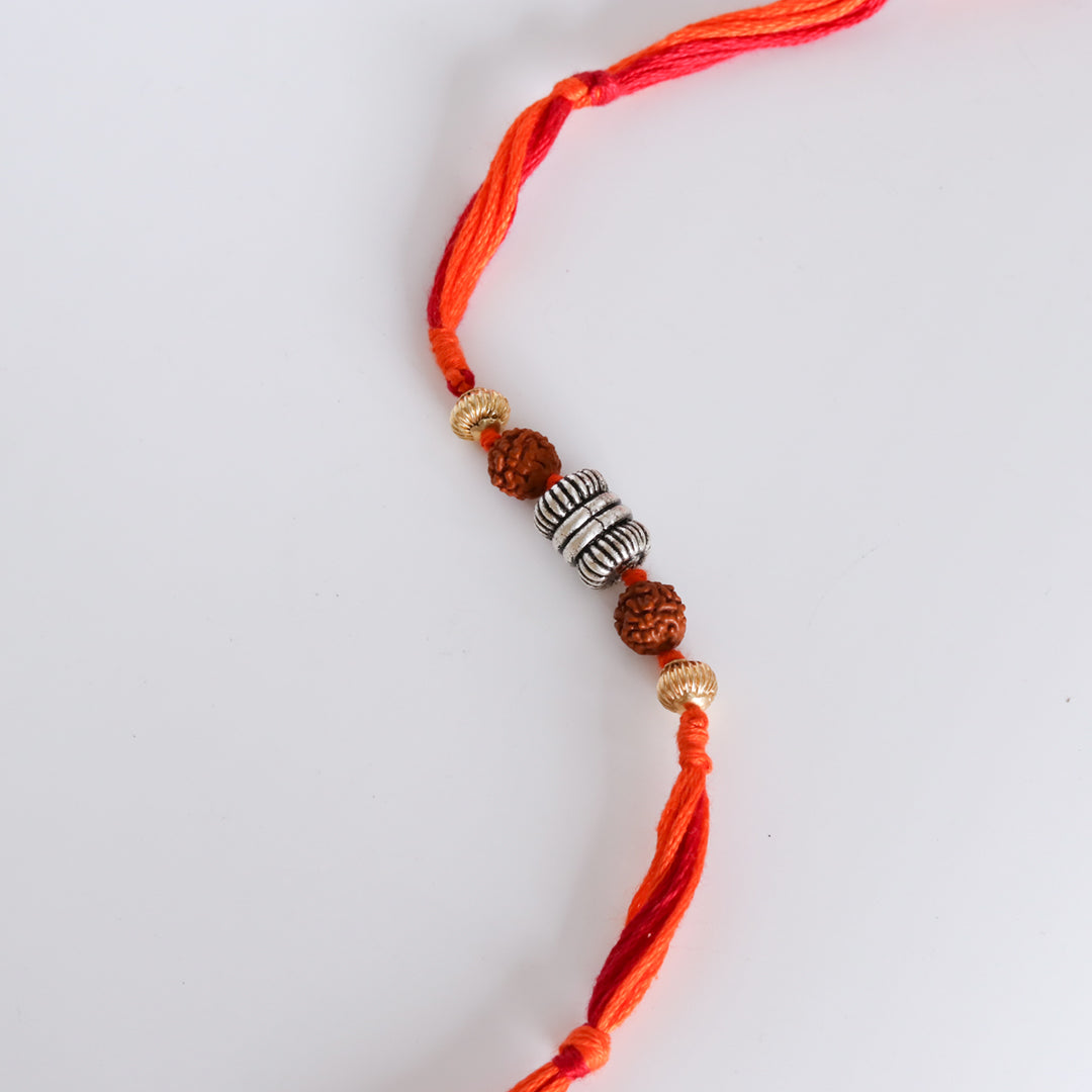 Rakhi close-up: red–orange thread with rudraksha beads, silver rings, and tassels