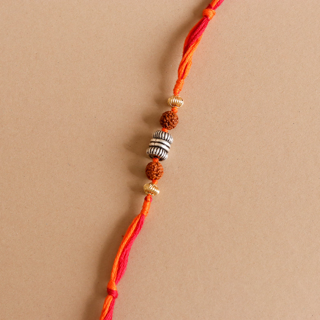 Rakhi close-up: red–orange thread with rudraksha beads and silver ribbed spacers