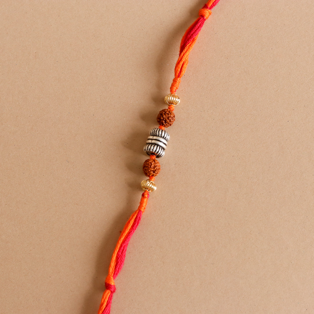 Rakhi close-up: red–orange thread with rudraksha beads and silver ribbed spacers