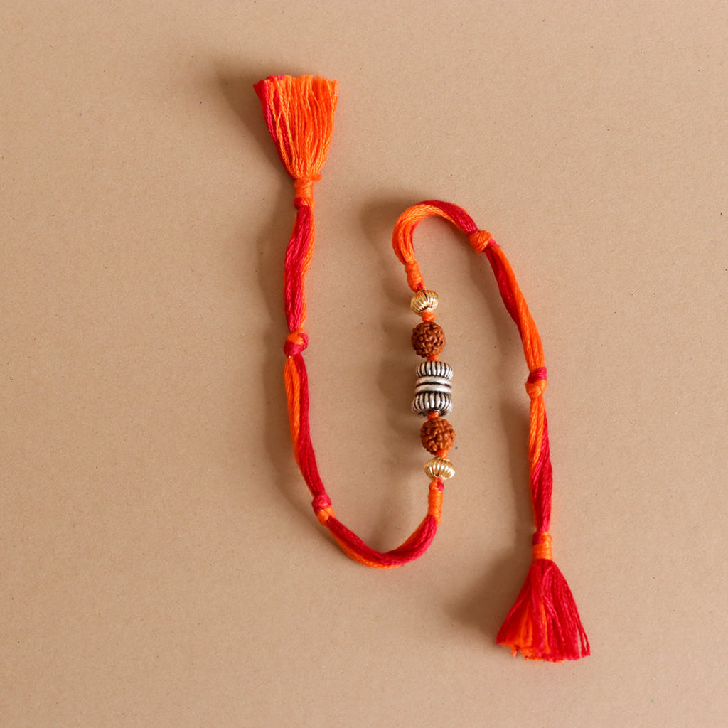 Rakhi bracelet with red–orange thread, tassels, rudraksha beads, and silver rings
