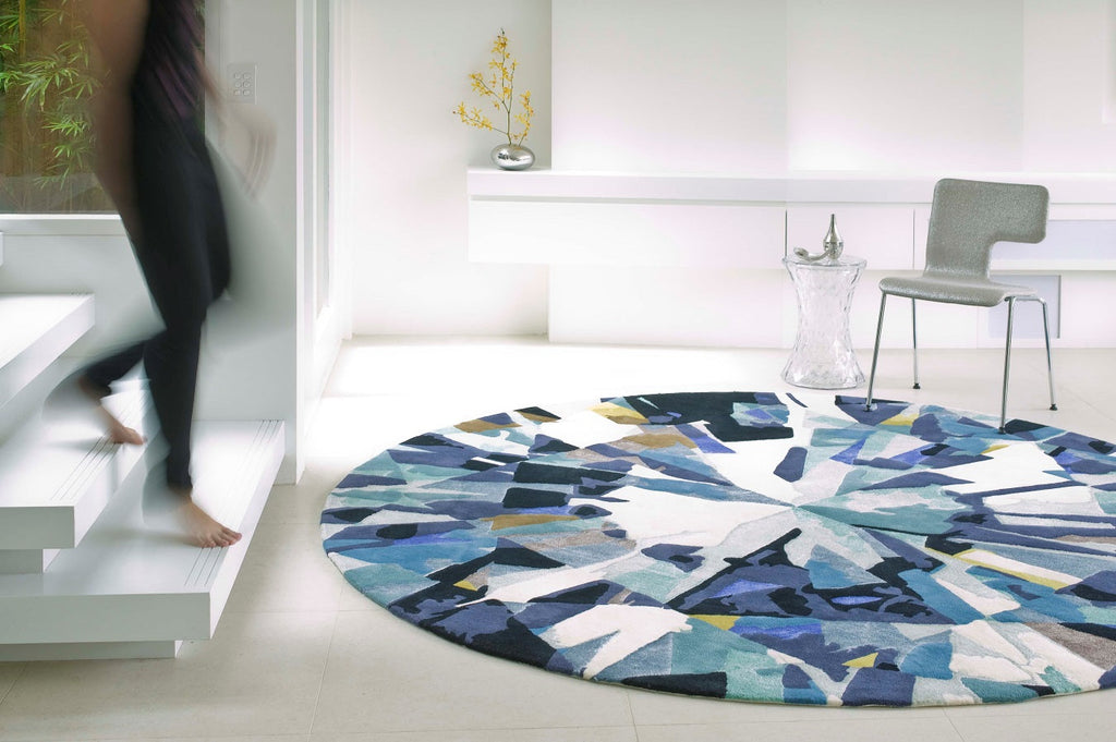 Round wool rug with angular blue and teal shapes over ivory field