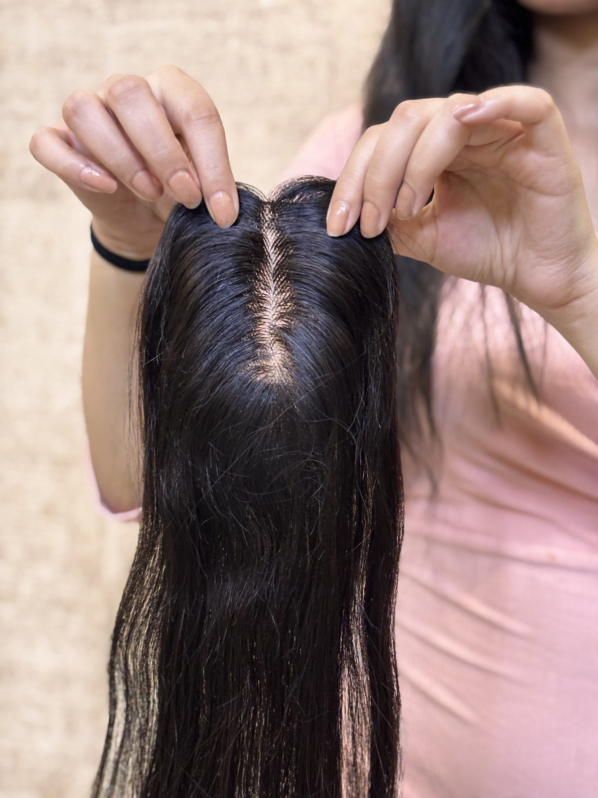 Natural black straight hair patch being held, showing center part and base blend.
