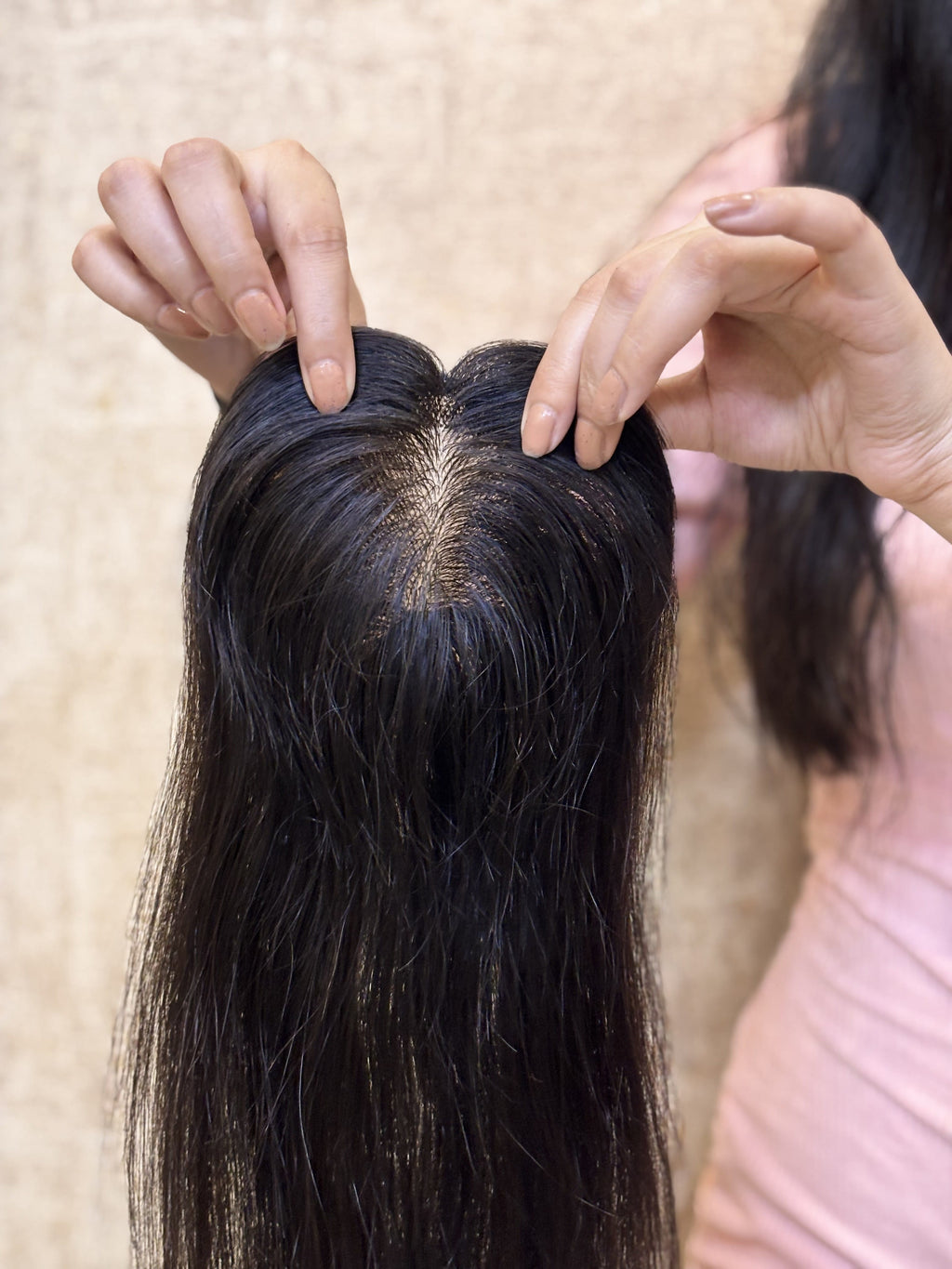Natural black straight hair patch with center parting and hands adjusting the base.